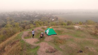 Genç bir ailenin, ebeveynlerin ve çocukların bahar dağlarında yürüyüş yaparken kamp çadırının yanında yürüdükleri hava manzarası. Aktif aile seyahati kavramı.