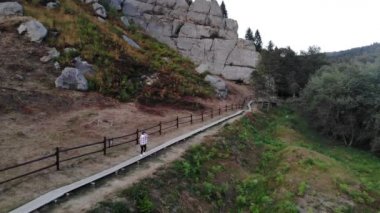 Ukrayna Karpatları 'nın ulusal parkında kayalar arasında tahta patikada yürüyen genç turist kadının hava manzarası. Ünlü Tustan kalesi tarihin ve mimarinin eşsiz bir anıtıdır.. 