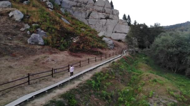 Vista aérea de la joven turista caminando por un sendero de madera entre rocas en el parque nacional de los Cárpatos Ucranianos. Famosa fortaleza de Tustán es un monumento único de la historia y la arquitectura. — Vídeos de Stock