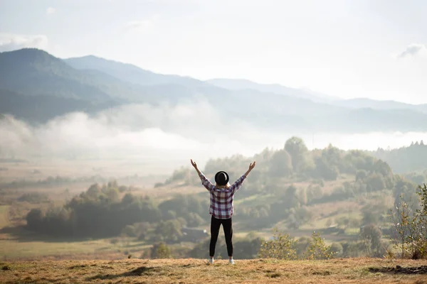 Chica feliz de pie en la cima de las montañas con los brazos levantados y disfrutar de una vista increíble. Senderista femenina silueta en la cima de la montaña de verano cubierta de nubes blancas. — Foto de Stock