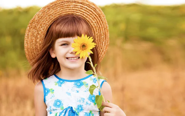 Hermosa niña en sombrero de paja con pelo aleteo ocultar ojo con girasol, caminar al aire libre en vacaciones de verano —  Fotos de Stock