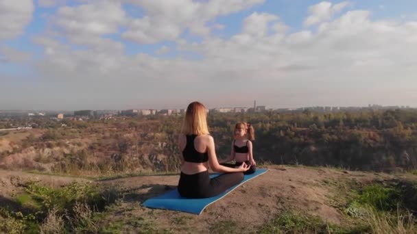 Familie pilates trainen samen. Jonge moeder en haar dochter doen yoga oefeningen op de top van de heuvel in de ochtend. Sport onderwijs en ontwikkeling van kinderen — Stockvideo