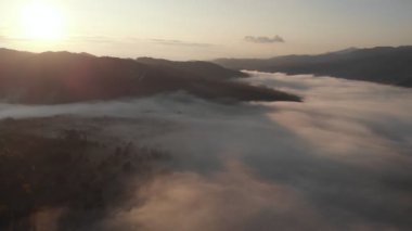 Bulutların ve gökyüzünün üzerinde sabah güneşinin doğuşu için harika bir hava aracı görüntüsü. Dağların tepesinde bulutlar arasında uçuyor. Güzel günbatımı dağ sırtı