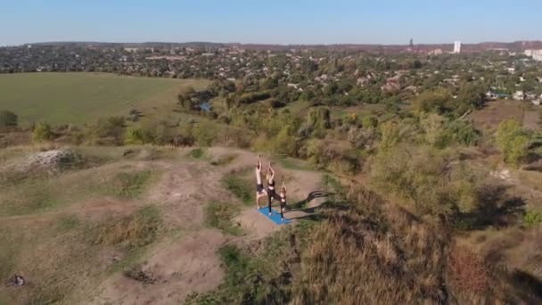 Luftaufnahme einer dreiköpfigen Familie, Mutter, Vater und Tochter, die an einem sonnigen Morgen auf einem Hügel Yoga-Übungen macht. Junge Familien bilden fernab der Hektik der Stadt aus, gehen mit gutem Beispiel voran und vermitteln — Stockvideo