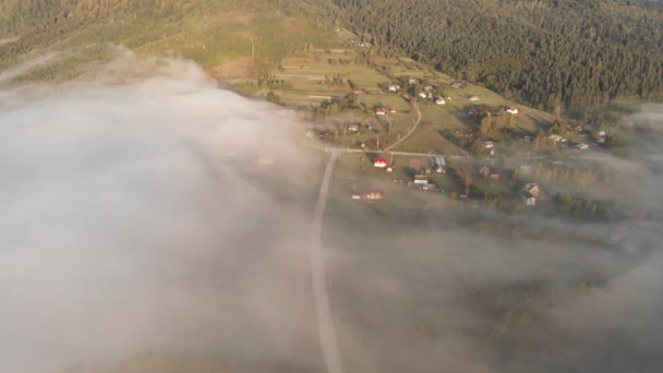 Lot z lotu ptaka nad chmurami między górami. Góry pokryte gęstą mgłą. Ciężka mgła wznosząca się nad lasem górskim wczesnym świtem. Mgliste chmury leżą na wzgórzach. — Wideo stockowe