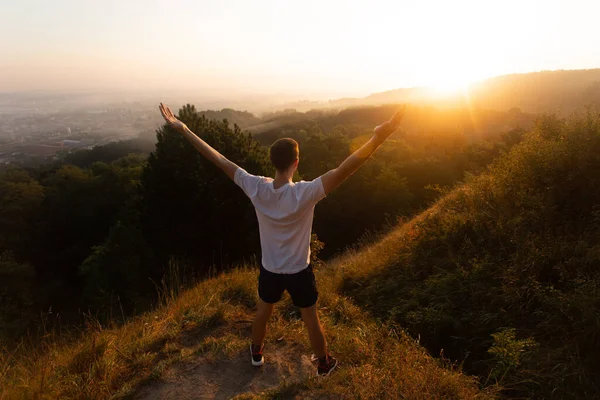 A fiatalember sziluettje felemeli a kezét napnyugtáig vagy napkeltéig a hegy tetején nyáron. — Stock Fotó