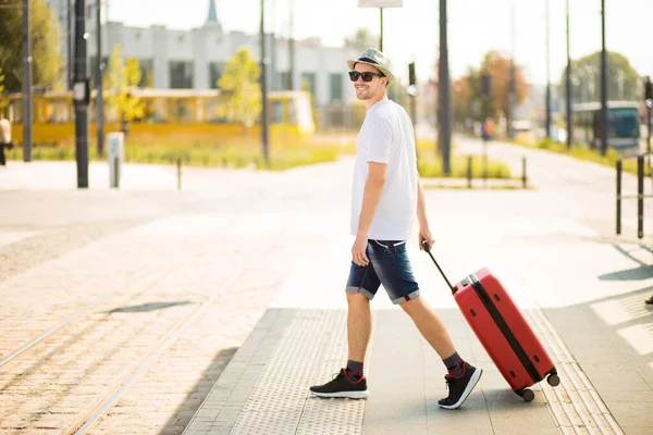 Beau jeune touriste barbu de lunettes de soleil roulant valise rouge à la gare. Concept de voyage et de vacances. Voyage. Espace de copie. — Photo