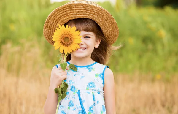 Schöne kleine Mädchen mit Strohhut mit flatterndem Haar verstecken Auge mit Sonnenblume, Wandern im Freien im Sommerurlaub — Stockfoto