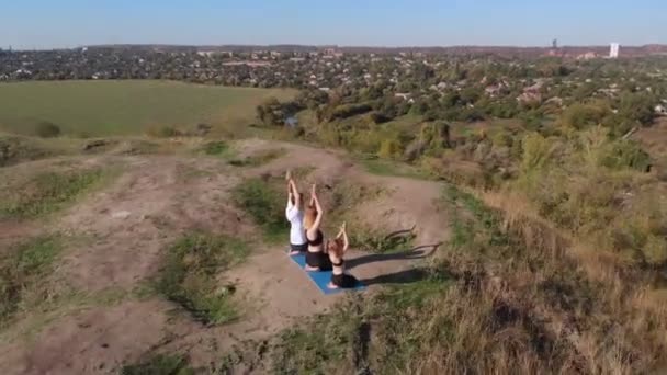 Orbitando tiro aéreo da família de três, pai e filha mãe, fazer exercícios de ioga no topo da colina na manhã ensolarada. Treinamento familiar jovem longe da azáfama da cidade, dar um bom exemplo e incutir em — Vídeo de Stock