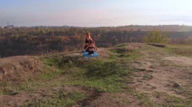İnce ve genç bir annenin hava aracı görüntüsü, sabah kızıyla birlikte yüksek tepelerde yoga egzersizleri yapıyor, şehrin telaşlı ortamından uzakta, iyi örnek oluyor ve sağlıklı alışkanlıklarını ona aşılıyor.