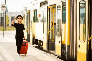 Siyah ve güneş gözlüklü genç bir bayan yolcu kırmızı tekerlekli bavullarını çekiyor ve yürüyor. Seyahat kavramı. Boşluğu kopyala
