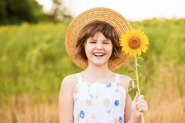 Belle petite fille en chapeau de paille avec des cheveux flottants avec des fleurs de tournesol, marchant en plein air pendant les vacances d'été — Photo