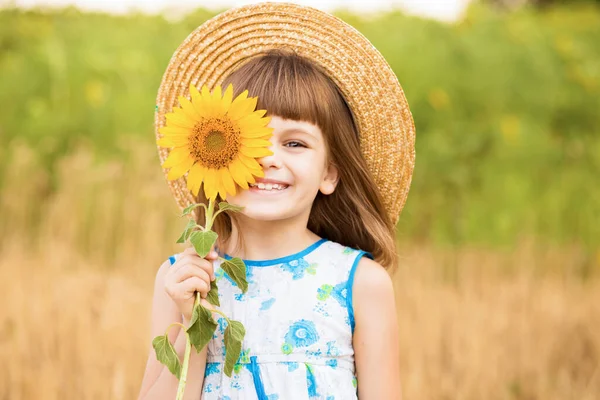 Hermosa niña en sombrero de paja con pelo aleteo ocultar ojo con girasol, caminar al aire libre en vacaciones de verano —  Fotos de Stock