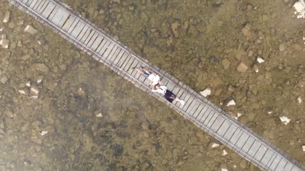Letecký pohled shora dolů na zamilovaný mladý pár ležící společně na dřevěném mostě přes řeku. — Stock video