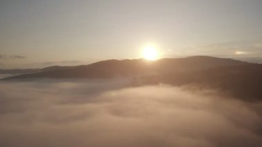 Bulutların ve gökyüzünün üzerinde sabah güneşinin doğuşu için harika bir hava aracı görüntüsü. Dağların tepesinde bulutlar arasında uçuyor. Güzel günbatımı dağ sırtı