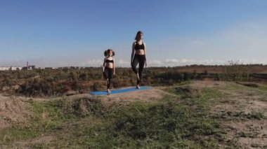 Aile pilates eğitimi. Genç anne ve kızı sabahları tepenin üstünde esneme egzersizleri yapıyorlar. Spor eğitimi ve çocuk gelişimi