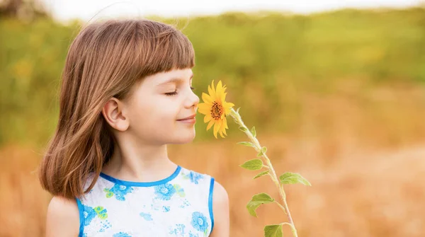 Menina adorável com fluttering cabelo segurar e cheirar girassol flor, andando ao ar livre em férias de verão — Fotografia de Stock