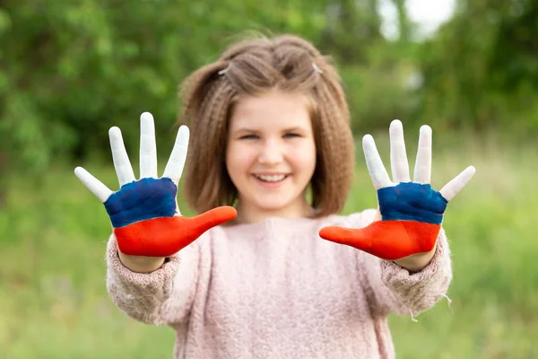 Niña mostrar las manos pintadas en Rusia colores de la bandera caminando al aire libre, centrarse en las manos. Día de la bandera rusa. Patriotas ciudadanos nacionalidad. 12 de junio. 22 de agosto vacaciones. 4 de noviembre Imagen De Stock