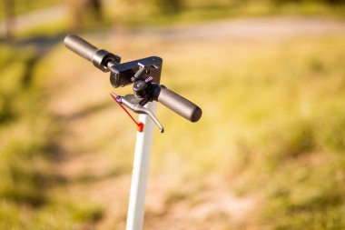 Yazın açık havada siyah saplı beyaz scooter 'ın seçici odak noktası. Ekranlı elektrikli scooter gidonu. Pil şarjı göstergesi