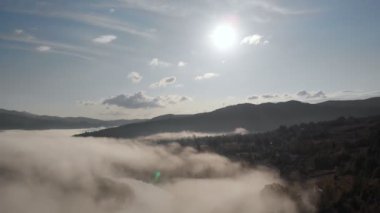 Alçak bulutlar üzerinde hava aracı uçuş manzarası ve güneş doğarken dağ yamaçlarını kaplayan sabah sisi. Dağlarda gün doğumu bulutlar.