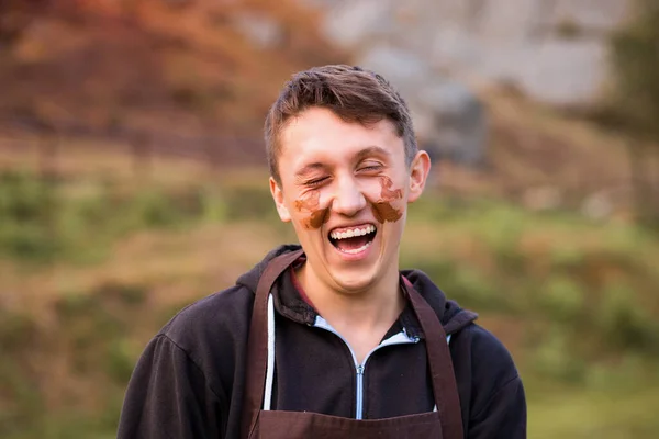 Радостный портрет человека-гончара с глиняным грязным лицом. Молодой красивый мужчина на керамической мастерской для детей. — стоковое фото