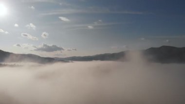 Alçak bulutlar üzerinde hava aracı uçuş manzarası ve güneş doğarken dağ yamaçlarını kaplayan sabah sisi. Dağlarda gün doğumu bulutlar.