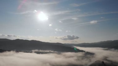 Alçak bulutlar üzerinde hava aracı uçuş manzarası ve güneş doğarken dağ yamaçlarını kaplayan sabah sisi. Dağlarda gün doğumu bulutlar.