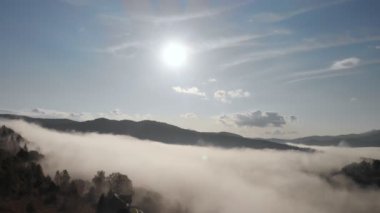 Alçak bulutlar üzerinde hava aracı uçuş manzarası ve güneş doğarken dağ yamaçlarını kaplayan sabah sisi. Dağlarda gün doğumu bulutlar.