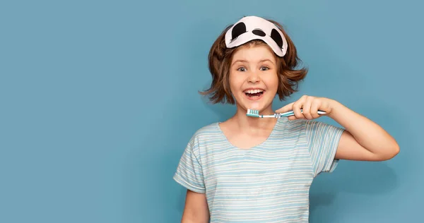 Ευτυχισμένο κορίτσι παιδί με μάσκα ύπνου βουρτσίστε τα δόντια της με οδοντόβουρτσα το πρωί απομονώνονται σε μπλε φόντο. Υγειονομική περίθαλψη, οδοντιατρική υγιεινή. Mockup, αντίγραφο χώρου — Φωτογραφία Αρχείου