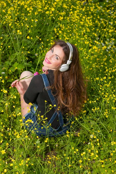 Hermosa joven con auriculares en las flores — Foto de Stock