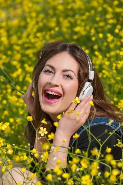 Hermosa joven con auriculares en las flores — Foto de Stock