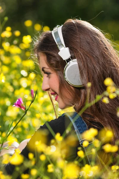 Menina bonita com fones de ouvido nas flores — Fotografia de Stock