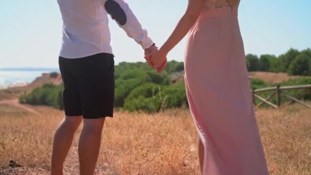 Ein junges Paar in einem romantischen Spaziergang am Meer, Blick auf die schöne Aussicht, Händchen haltend. — Stockvideo
