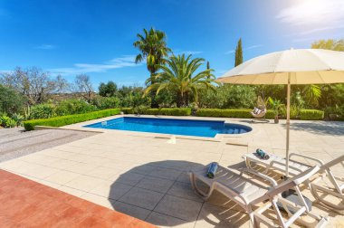 Özel bir villanın bahçesinde lüks bir havuz, tatil turistleri için yastıklı sallanan sandalye. Portekiz, Algarve.