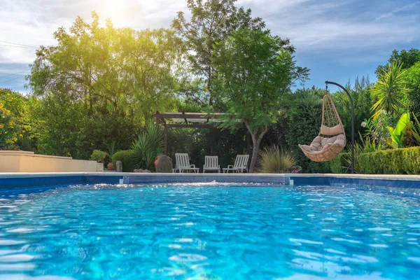 Lujosa piscina en el jardín de una villa privada, silla colgante con almohadas para turistas de ocio, en verano. Portugal, Algarve. Imágenes De Stock Sin Royalties Gratis