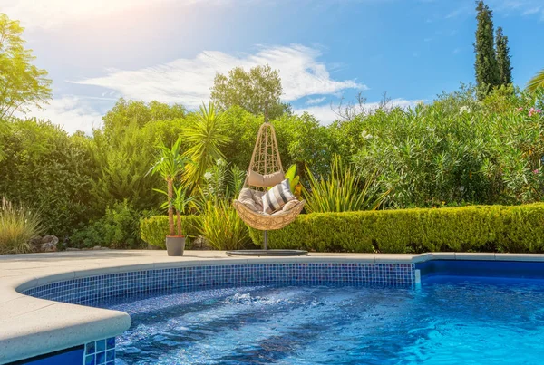 Lujosa piscina en el jardín de una villa privada, silla colgante con almohadas para turistas de ocio, en verano. Portugal, Algarve. Imagen De Stock