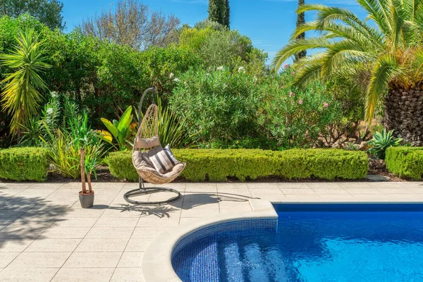 Lyxig pool i trädgården i en privat villa, hängande stol med kuddar för fritidsturister, på sommaren. Portugal, Algarve. — Stockfoto