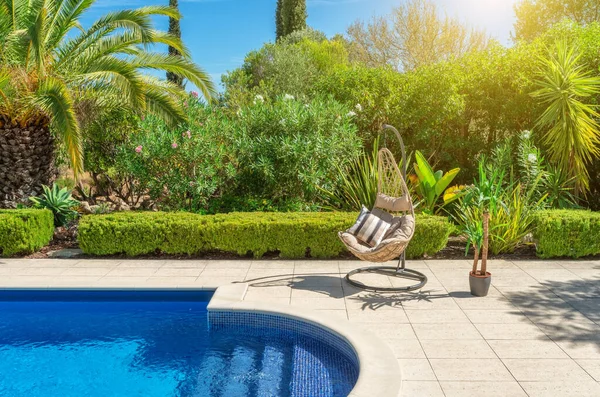 Luxurious pool in the garden of a private villa, hanging chair with pillows for leisure tourists, in summer. Portugal, Algarve.