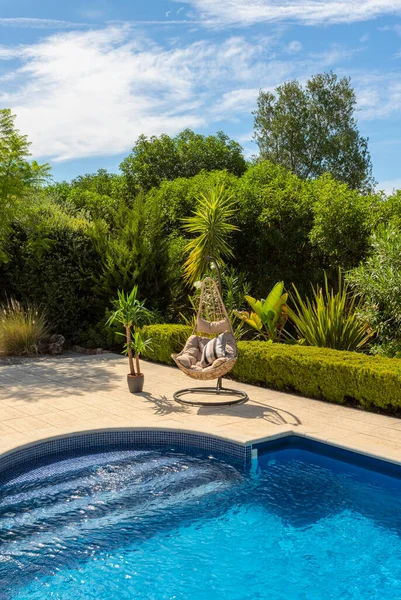 Lujosa piscina en el jardín de una villa privada, silla colgante con almohadas para turistas de ocio, en verano. Portugal, Algarve. Fotos De Stock Sin Royalties Gratis