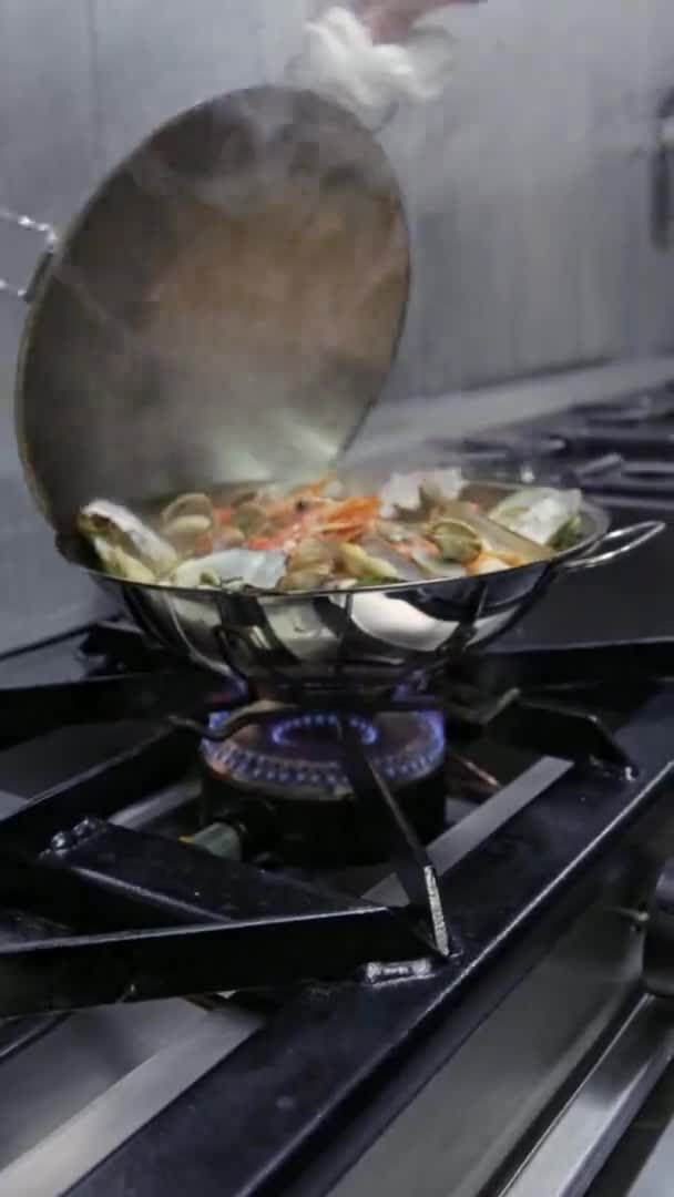 O chef remove a tampa da cataplan, que é cozinhada em um fogão a gás. Vídeo vertical. Close-up. — Vídeo de Stock