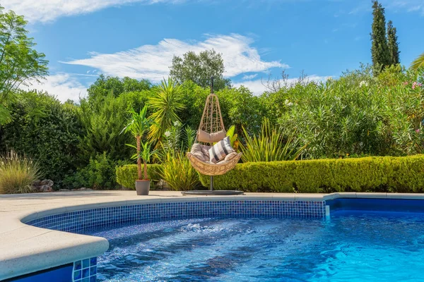 Luxurious pool in the garden of a private villa, hanging chair with pillows for leisure tourists, in summer. Portugal, Algarve.