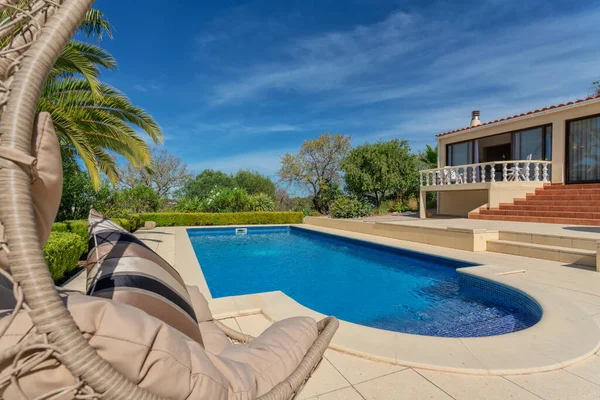 Lujosa piscina en el jardín de una villa privada, silla colgante con almohadas para turistas de ocio, en verano. Portugal, Algarve. Imagen De Stock