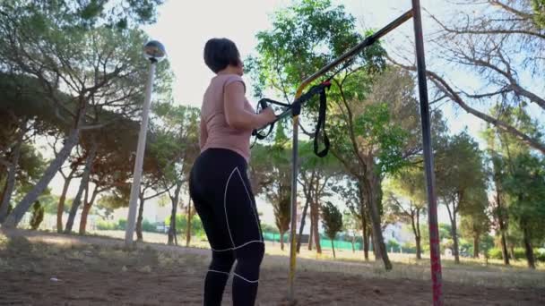 En brunett portugisisk kvinna, medelålders, gör en remmar squat, i en park på en solig morgon. — Stockvideo