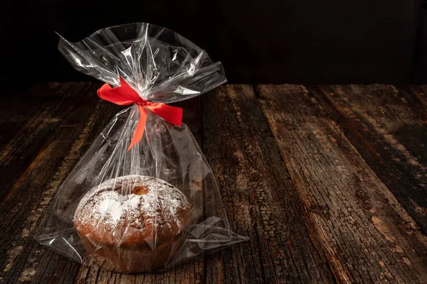 Stollen rye bread, round, packed in a plastic bag, on a wood textured background. With a red ribbon.