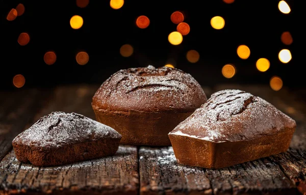 Trzy bożonarodzeniowe chleb, stollen, na drewnianym stole teksturowanym, na tle rozmytych świateł w bokeh. — Zdjęcie stockowe