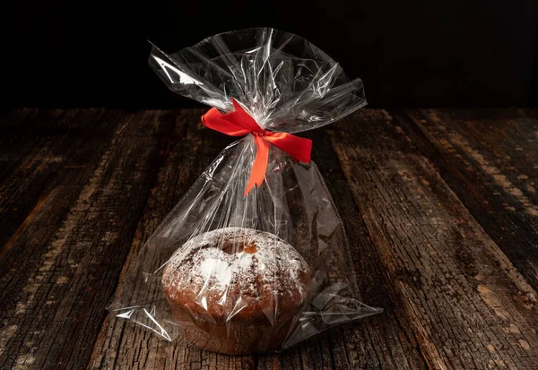 Pan de centeno tostado, redondo, envasado en una bolsa de plástico, sobre un fondo texturizado de madera. Con una cinta roja. — Foto de Stock