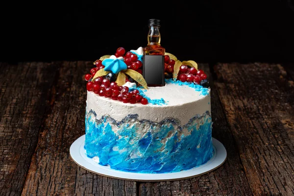 Gâteau à la crème aux fruits avec une bouteille de cognac, sur un fond texturé en bois. — Photo