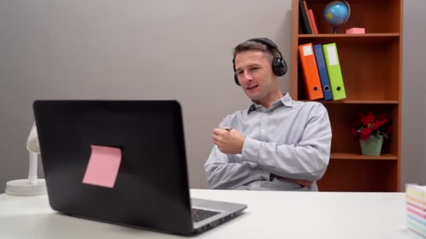 Un joven trabaja desde casa, dirige una conferencia en línea con el jefe y los empleados. — Vídeo de stock