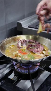 Şef ahtapot, deniz ürünleri ve sebzelerle mancınık pişiriyor. Dikey video. Yakın plan..