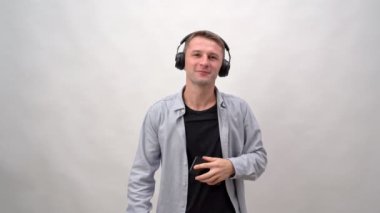 Kulaklıklı ve akıllı telefonlu beyaz arka planda müzik ve dans dinleyen genç bir adam. Duygularla dolu, Avrupa kökenli..